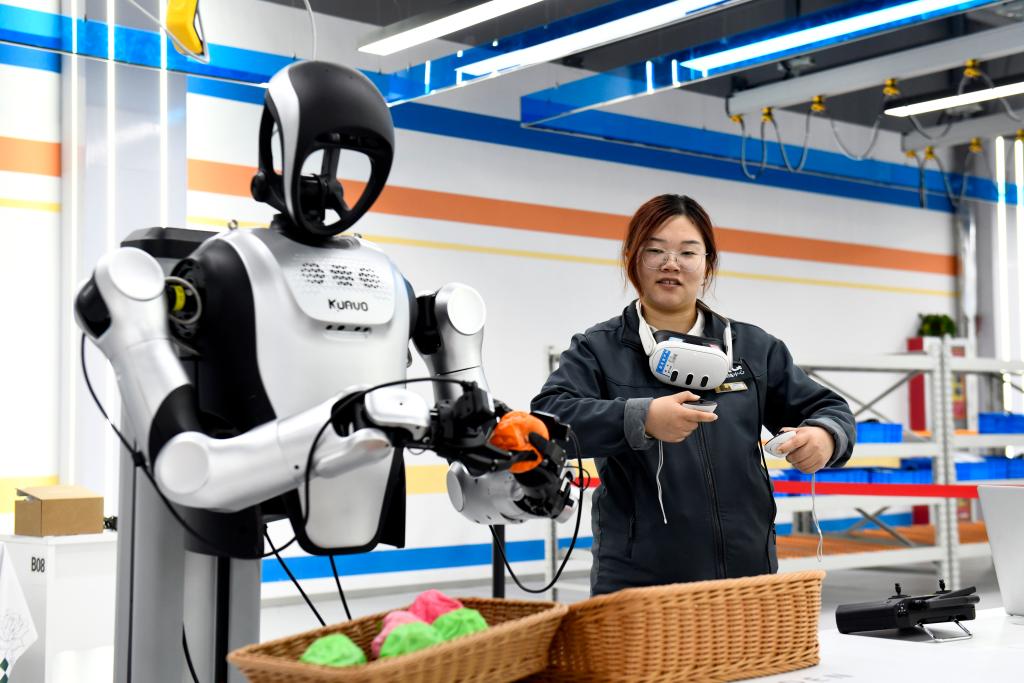 Uma treinadora supervisiona o treinamento de um robô humanoide em um cenário de limpeza doméstica em um centro de treinamento de dados para IA incorporada no distrito de Pingyin, na Província de Shandong, no leste da China, em 21 de abril de 2026. (Xinhua/Guo Xulei)
